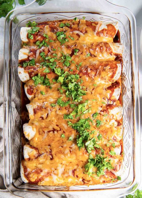 Baked enchiladas in baking dish garnished with fresh cilantro.
