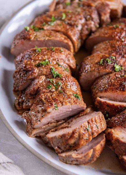 Close up of sliced pork tenderloin on a white serving plate.